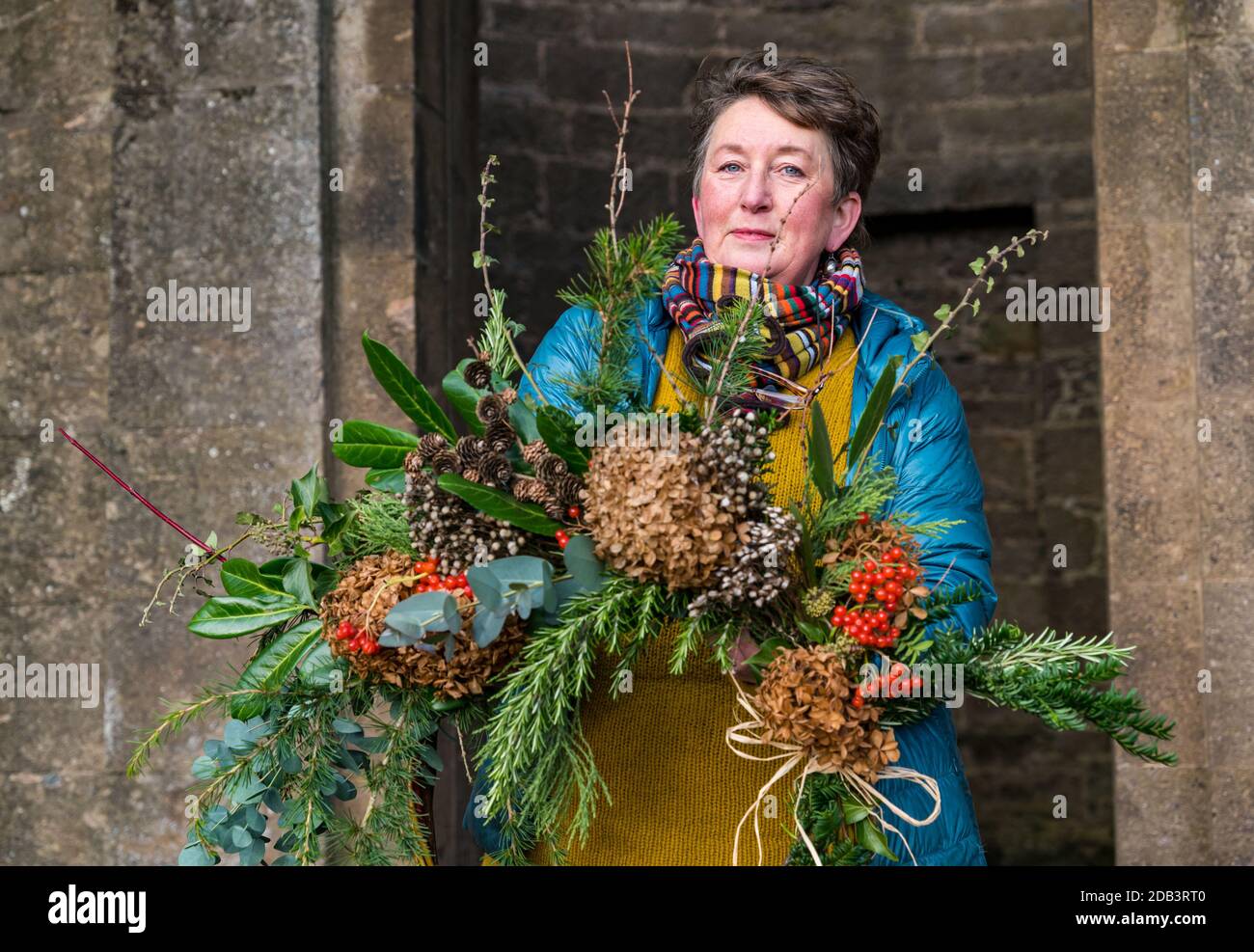 Haddington, East Lothian, Scotland, UK, Flowersmith prepares for Christmas:  Ruth Alder, a flower smith, weaves willow into wreaths to decorate for Christmas using foliage and flowers from Amisfield Walled Garden where she is a volunteer. Amisfield Walled garden is an 18th century garden managed by the Amisfield Preservation Trust and is free to visit all year round. Pictured: Ruth with a finished decorated Christmas wreath Stock Photo