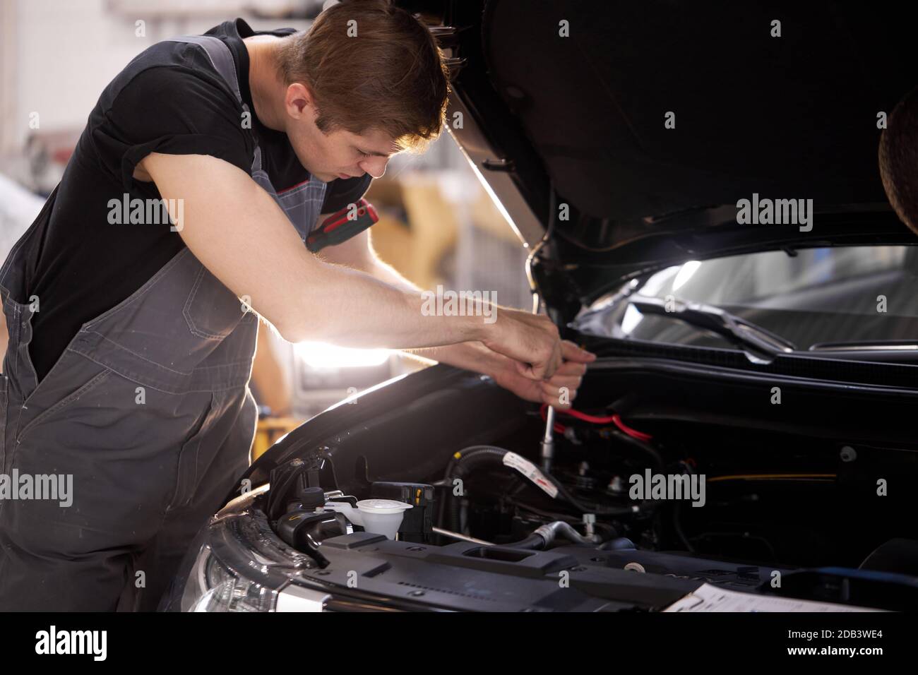 handsome guy repairing auto's hood, using tools. wearing unifrom