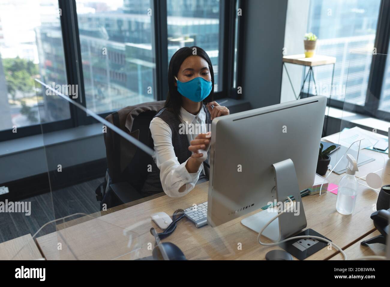 Asian woman wearing face mask using computer while sitting on her desk ...