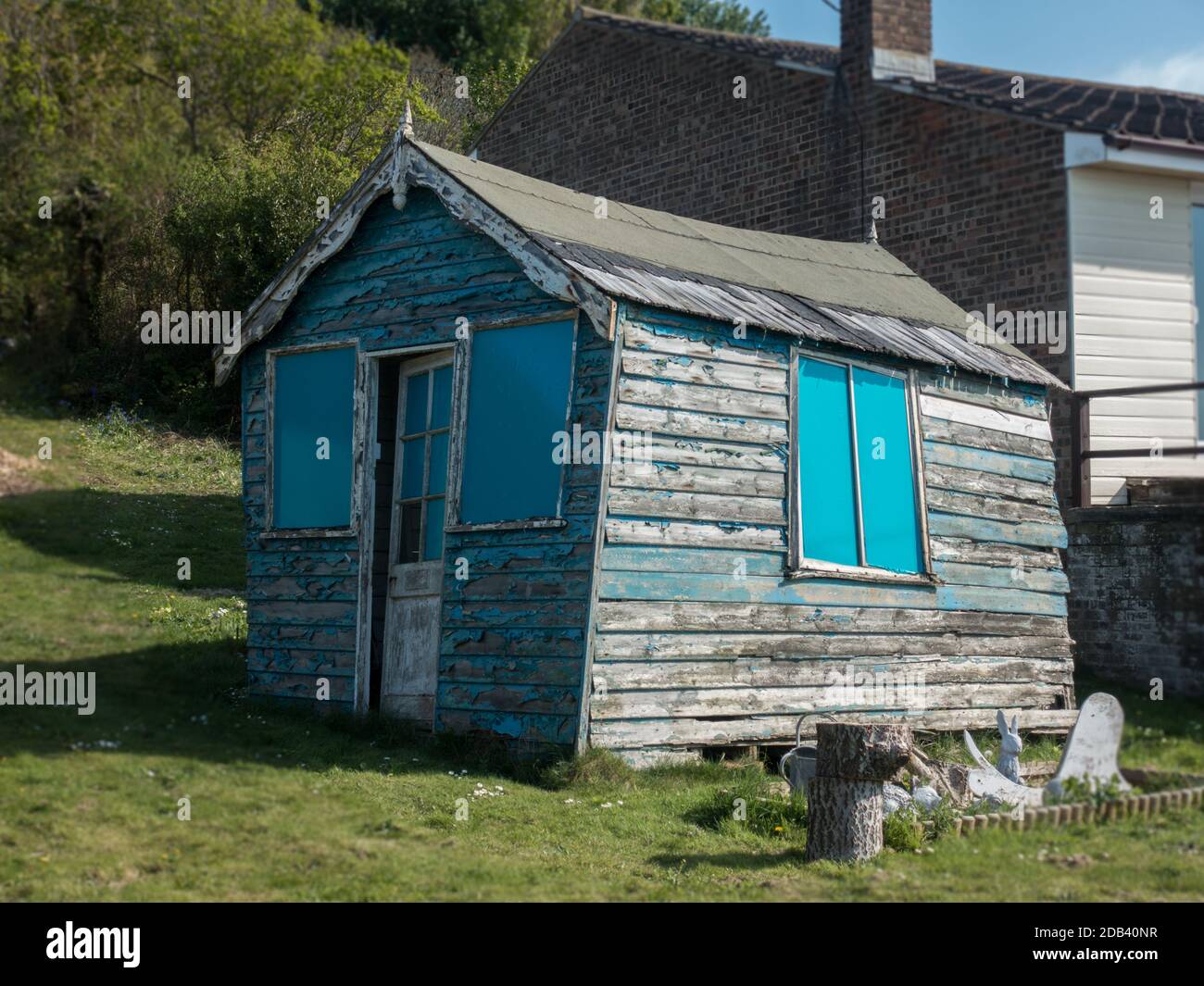 Abandoned derelict bending twisting contorting outside garden shed on grass with blue shutters blue sky sunny day Stock Photo