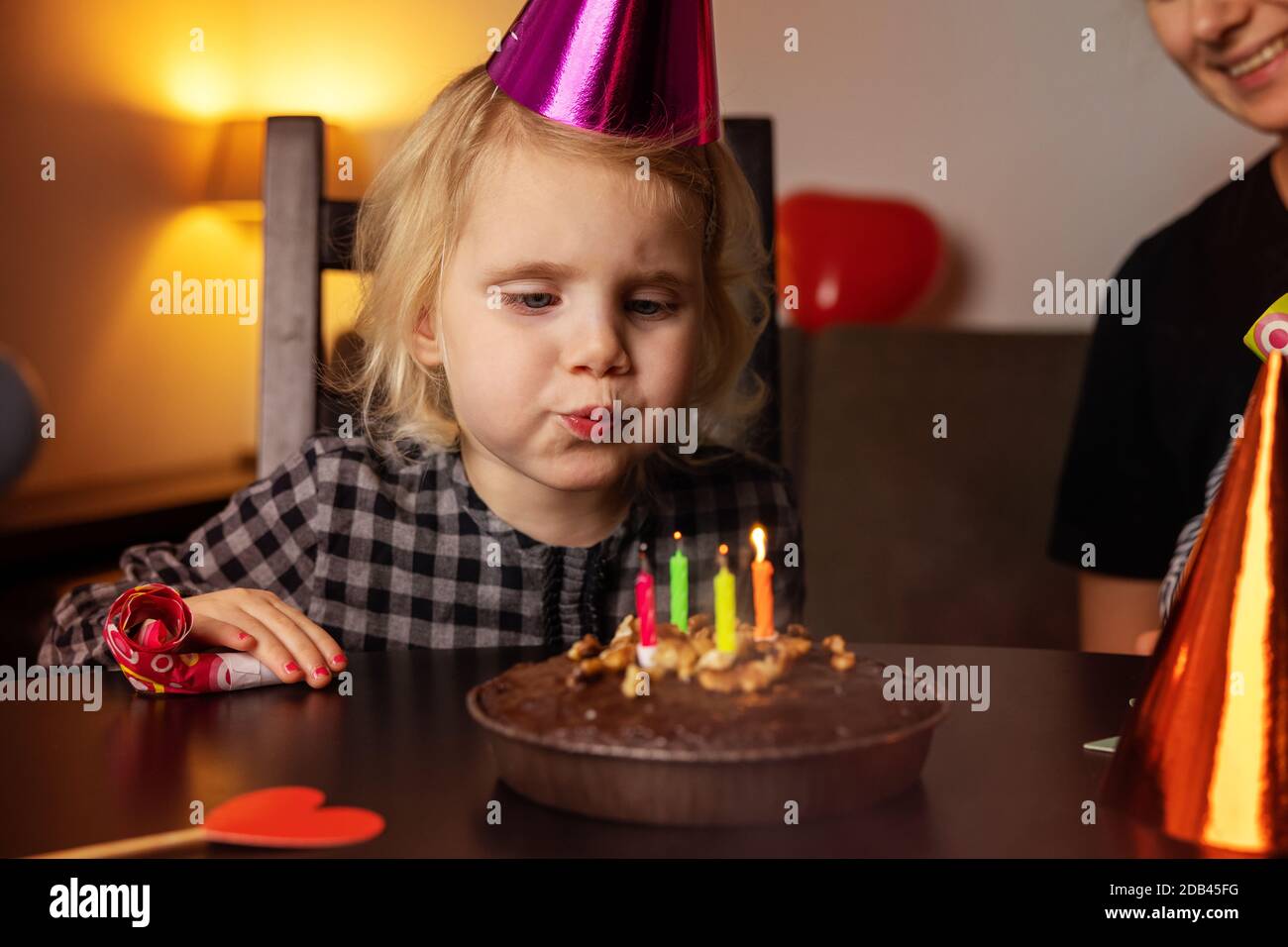 little girl with party hat blow out the candles on her birthday cake Stock Photo