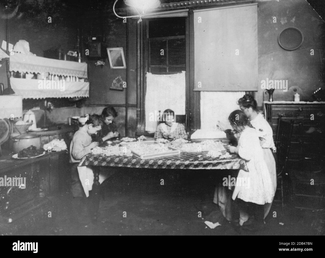 Night scene. 7:30 P.M. January 29, 1912. Making violets, and they often work later. Pollinni family, 5 Carmine St., N.Y. living in a rear [i.e., rear.] tenement. The six year old helps some. The eight, ten, and twelve year olds work later than this at times. Brothers, 15 and 17 years old, work in factory.. Stock Photo