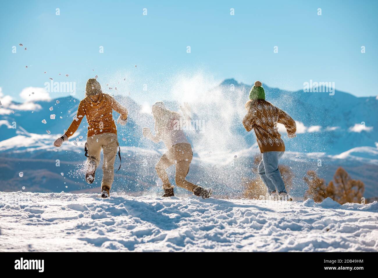 Three young happy girls friends are having fun in snow fight in mountains. First snow and winter vacations concept Stock Photo