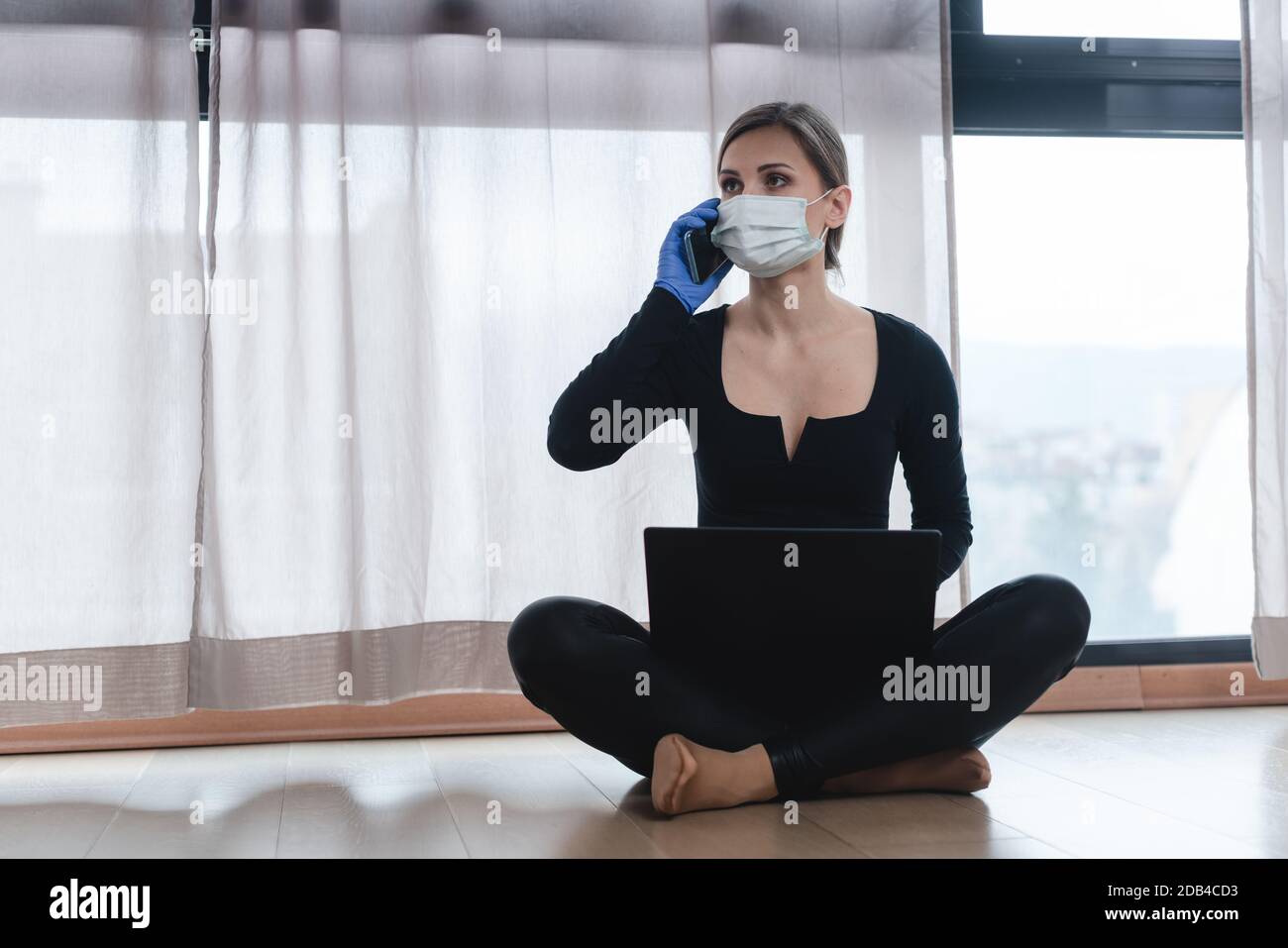 Woman in corona quarantine with phone and laptop on her floor Stock Photo