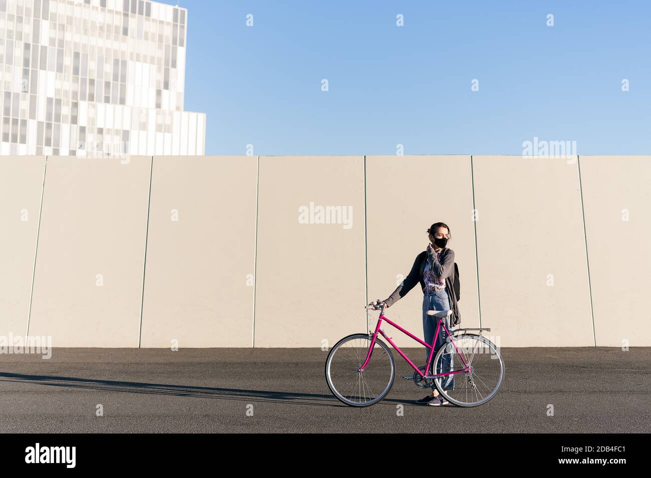 young girl with a pink retro bike at city adjusting her protective mask, concept of active lifestyle, protection against covid and sustainable urban m Stock Photo