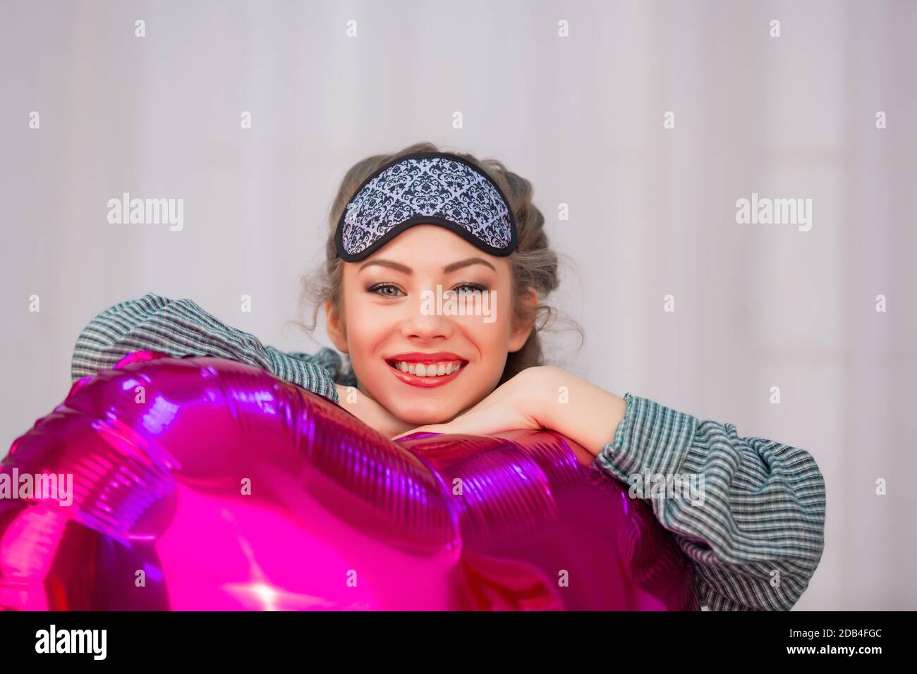 Young woman in sleep mask hugs pink heart-shaped balloon and smiles Stock Photo