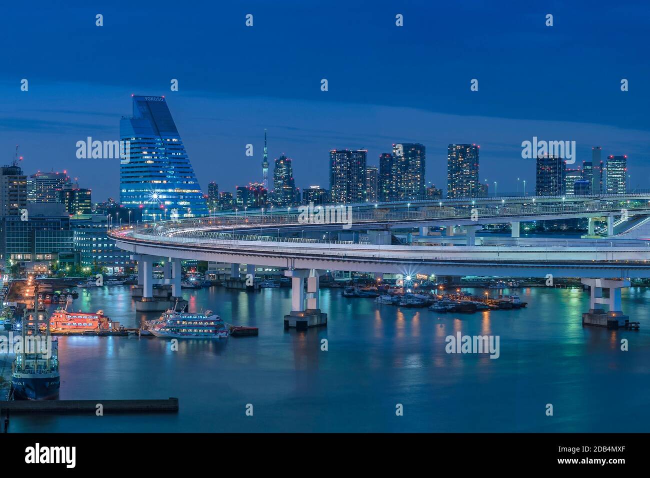 Circular highway leading to the Rainbow Bridge with Cargo and cruise ships moored or sailing in Odaiba Bay of Tokyo. Stock Photo