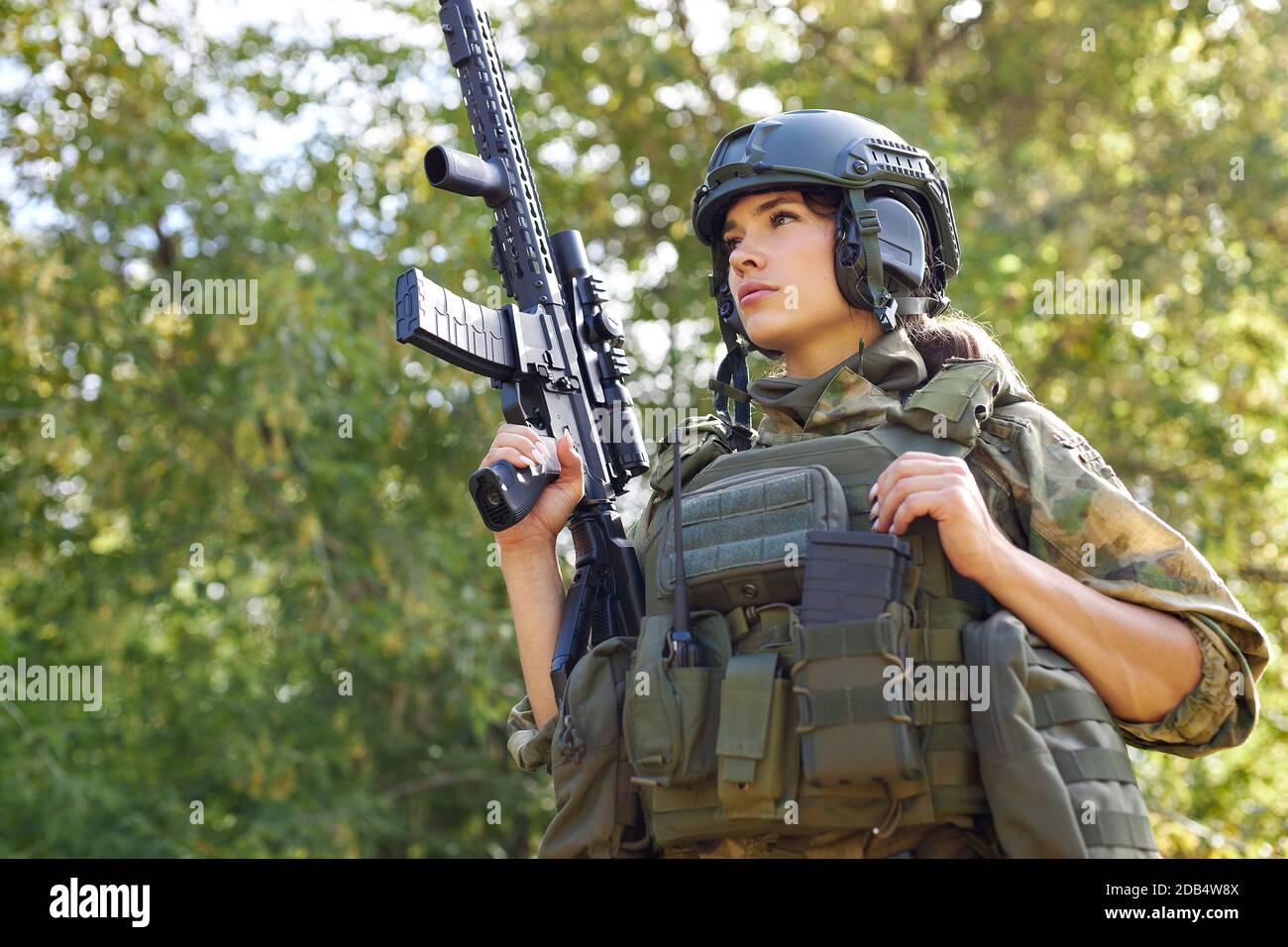 strong brave female army soldier with rifle machine gun standing in the forest, she is ready to shoot at enemy, firearm outdoor shooting range Stock Photo