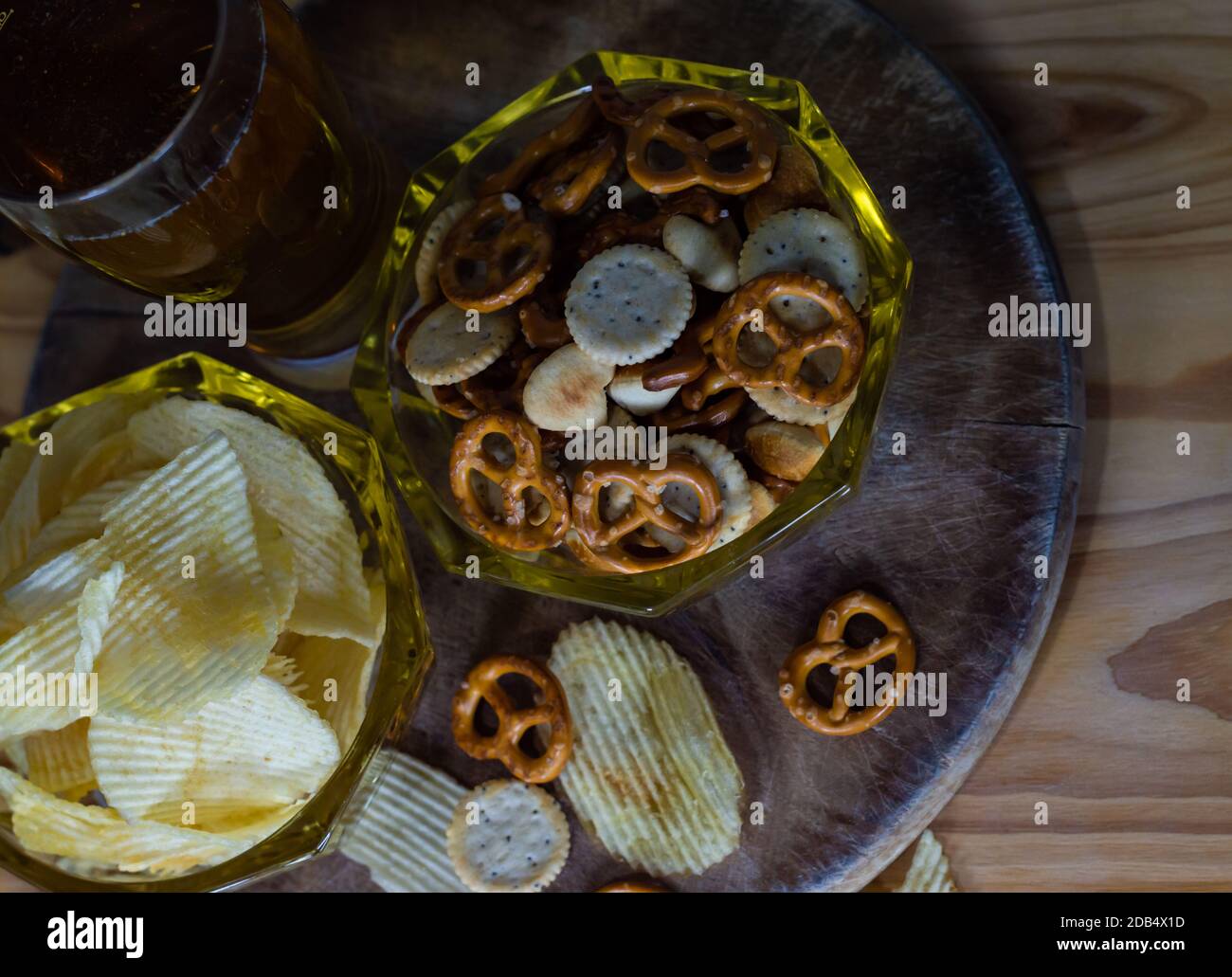 Cold beer and wavy potato chips in a bowl and salty snacks pretzel on a wood table Stock Photo
