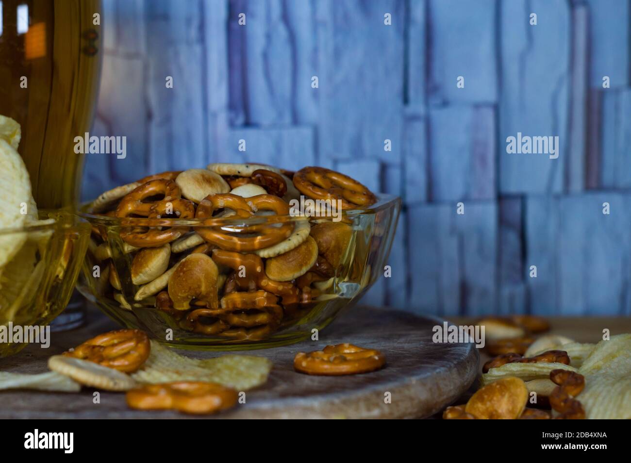 Cold beer and wavy potato chips in a bowl and salty snacks pretzel on a wood table Stock Photo