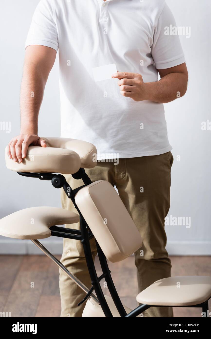 Cropped view of masseur standing near massage chair and holding blank business card Stock Photo