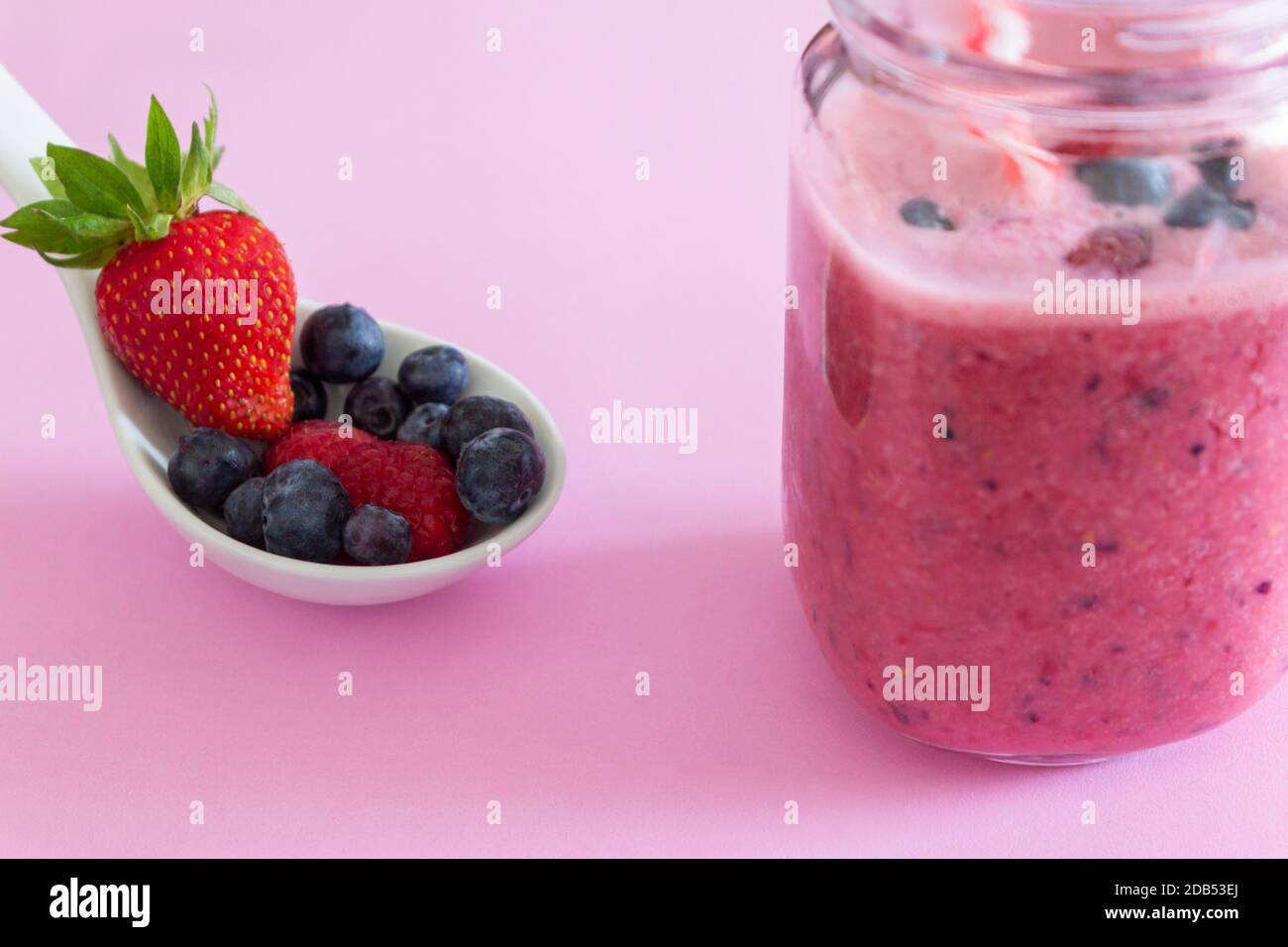 Pink strawberry smoothie with fresh fruits (strawberry, blueberries and raspberries)in a spoon on pink background.Healthy natural fruits juice drink c Stock Photo