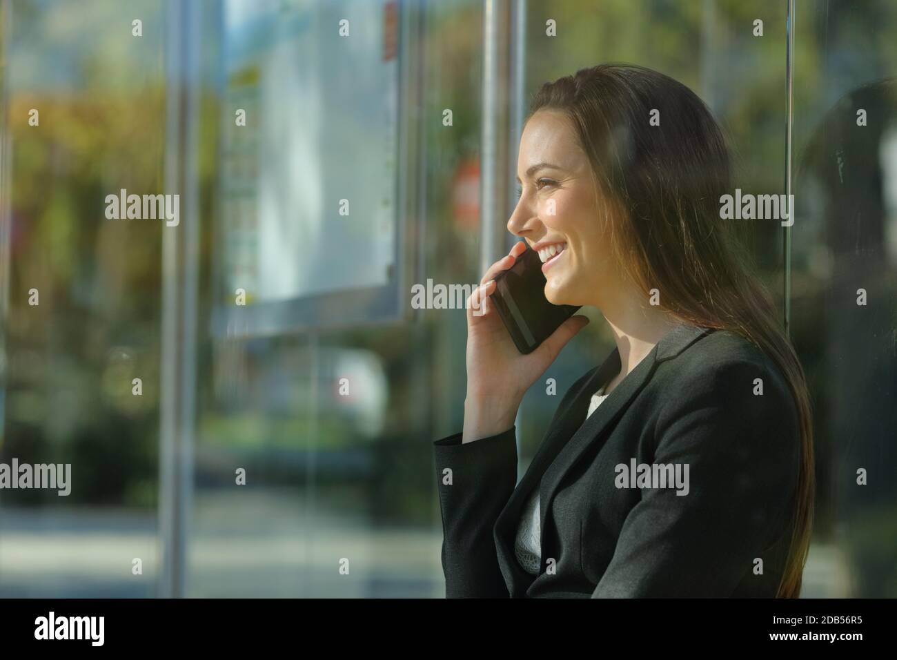 Profle of a happy executive woman talking on smart phone waiting on a bus stop Stock Photo