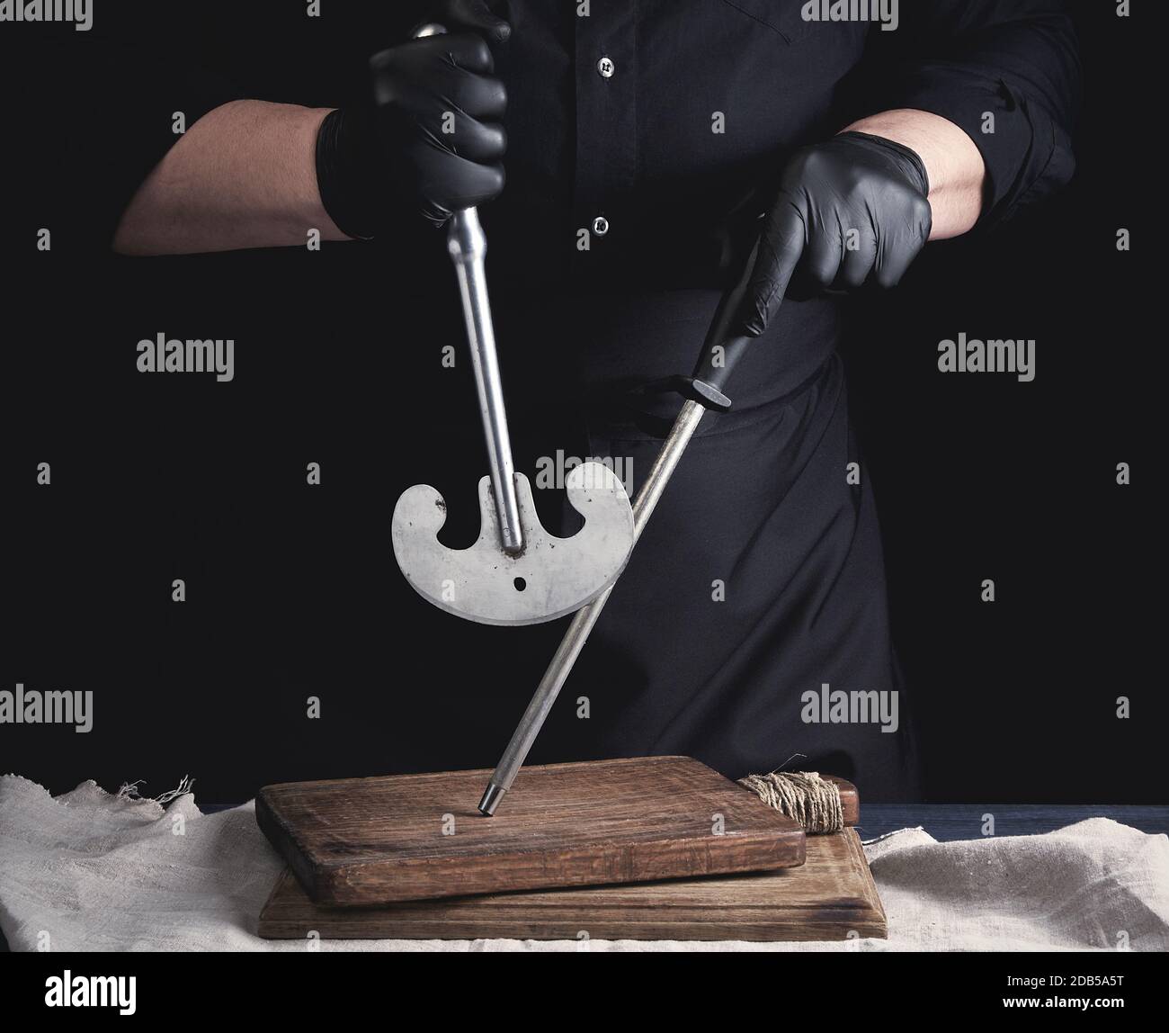 male cook in black uniform and black latex gloves holds a large sharp