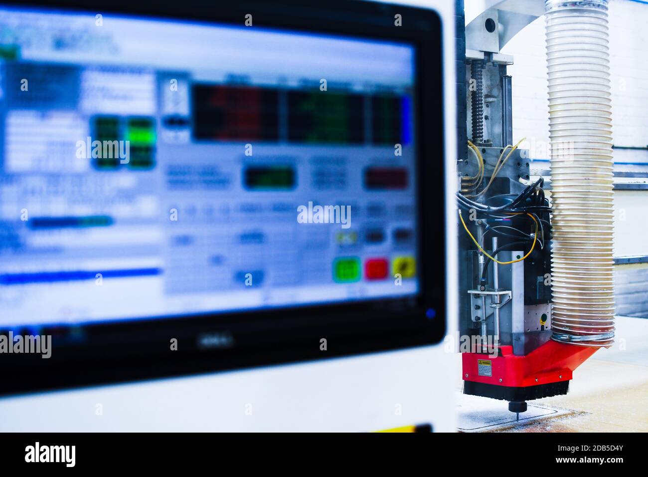 High speed plastic CNC machine pictured with the computer screen in foreground while cutting out a plastic shape in a factory. Stock Photo