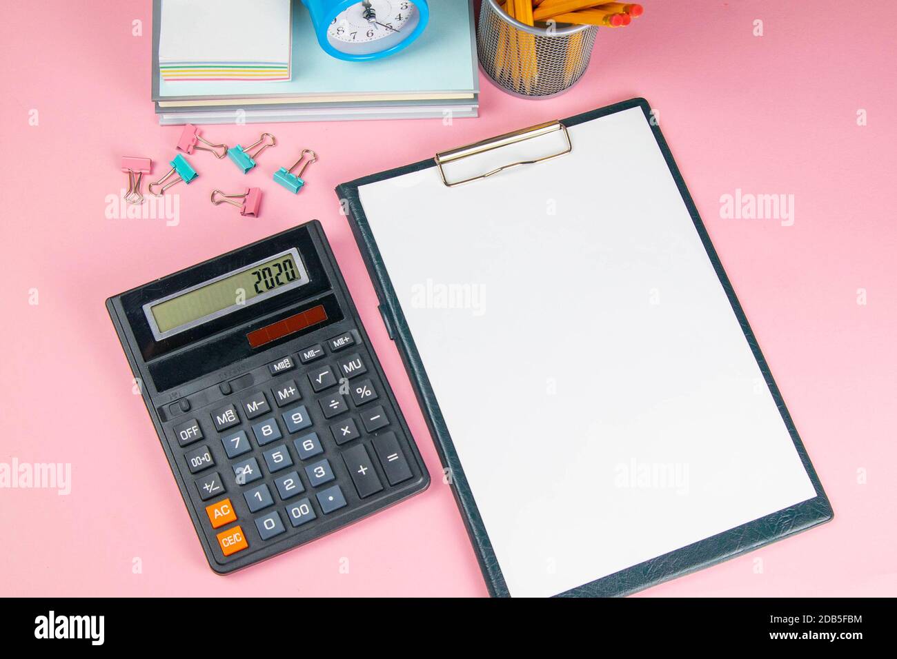On the pink table there is a calculator and a tablet with a white sheet, next to sprinkled clothespins for paper. Stock Photo