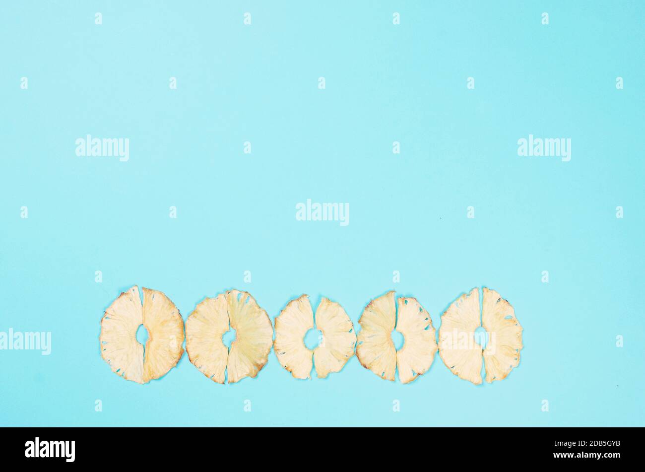 Dried pineapple wedges scattered on blue background. Fruit chips
