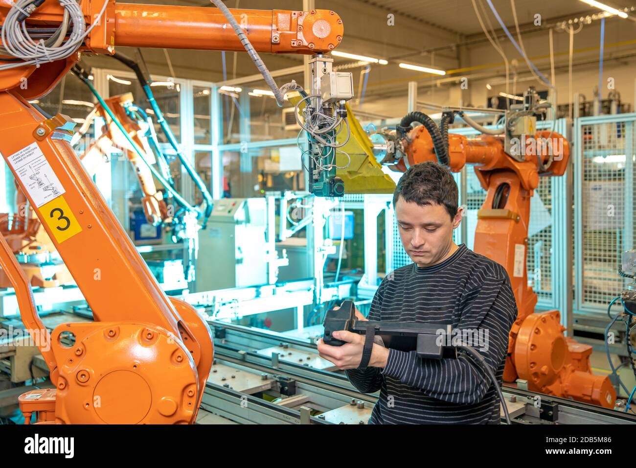 production engineer programs the robotic arms on the production line in a factory. Stock Photo