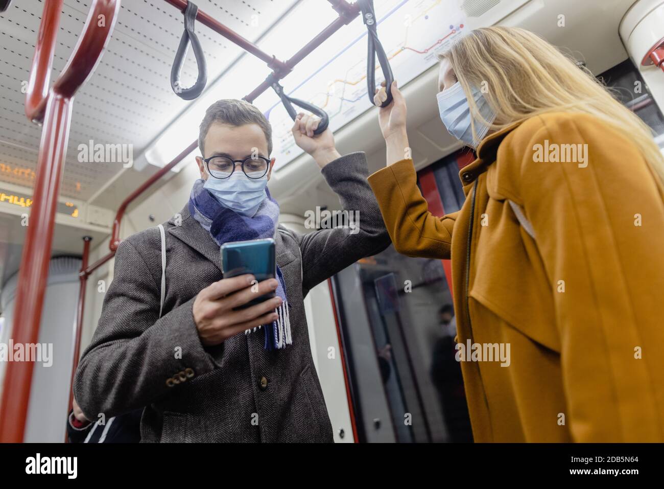People using phone in train wearing covid-19 face mask Stock Photo
