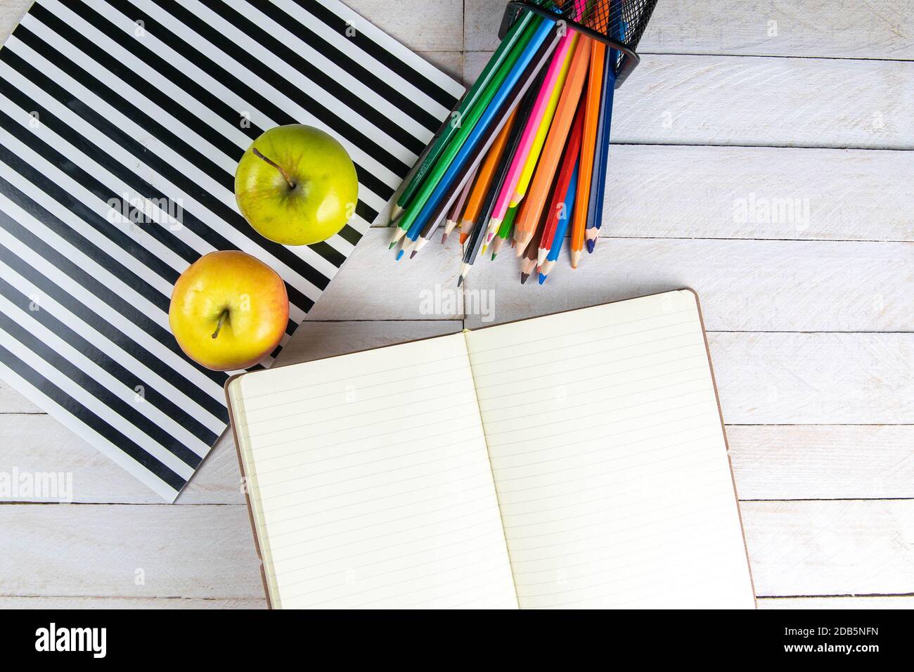 Top view of open notebook with empty pages, pencil and red apples on wooden table in office workspace. Stock Photo