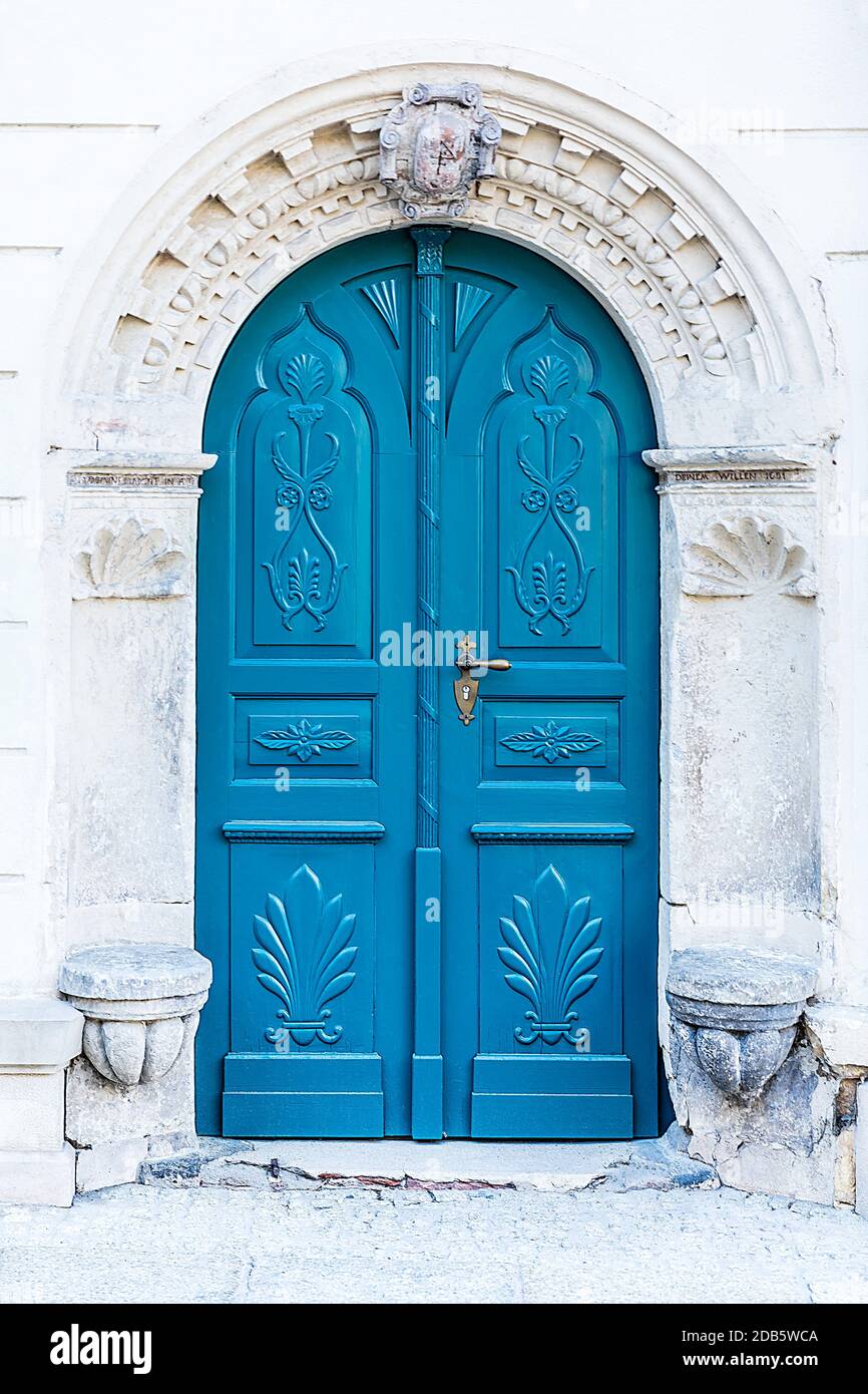 Historic entrance portal with a weathered coat of arms. Archway richly decorated with ornaments with a double-leaf blue wooden door. Stock Photo