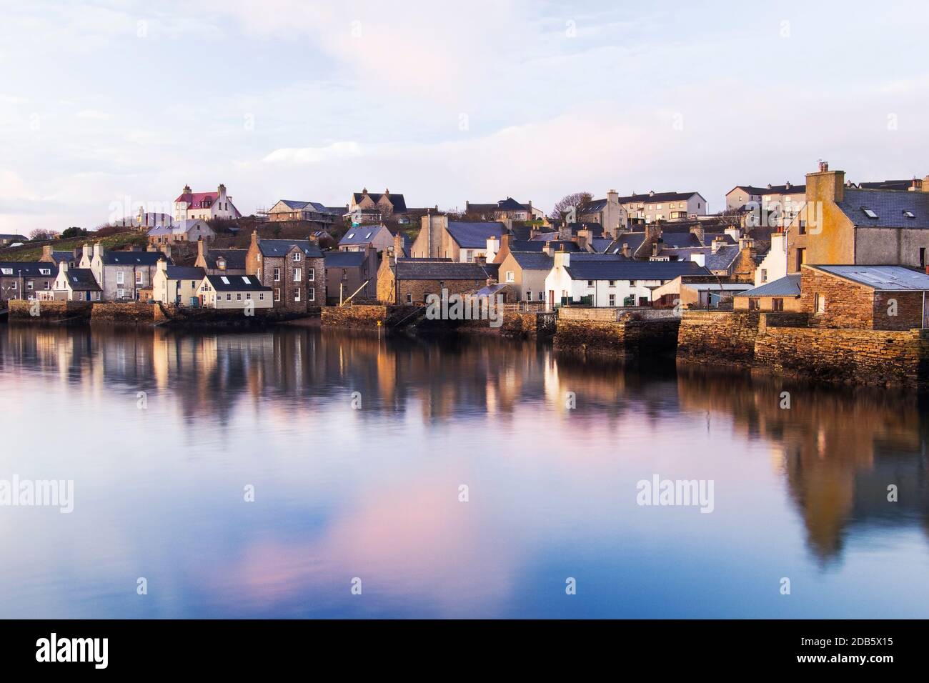 Morning light in waterfront view of Stromness harbour with white houses and reflections in water Stock Photo