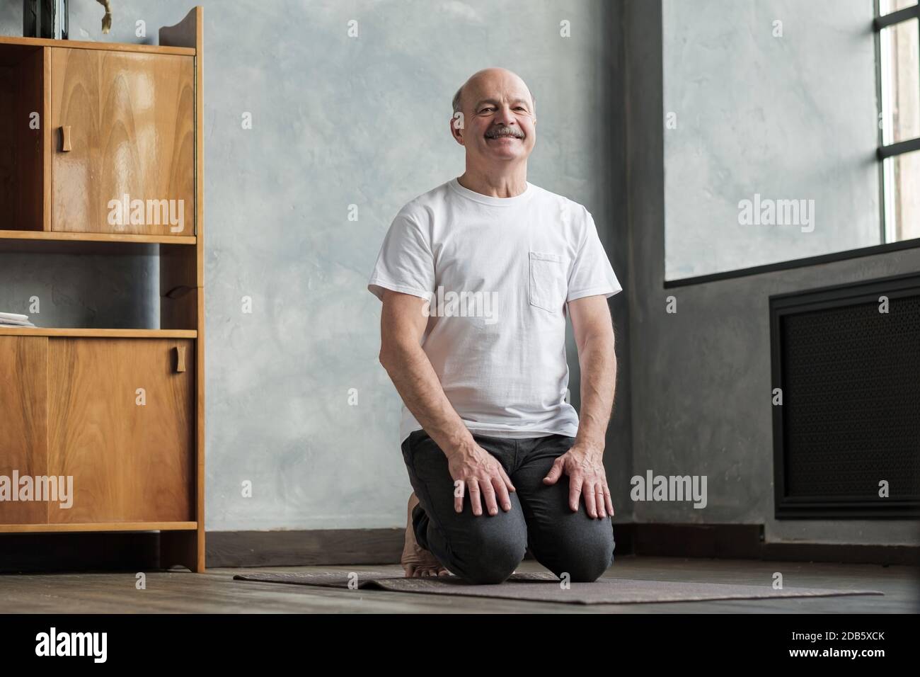 Senior man practicing yoga at home sitting in Vajrasana pose. Stock Photo