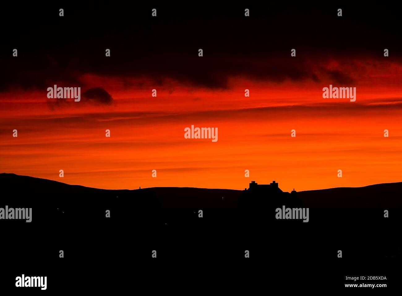 House and hills silhouettes on orange sunrise sky and black foreground on Orkney islands Stock Photo