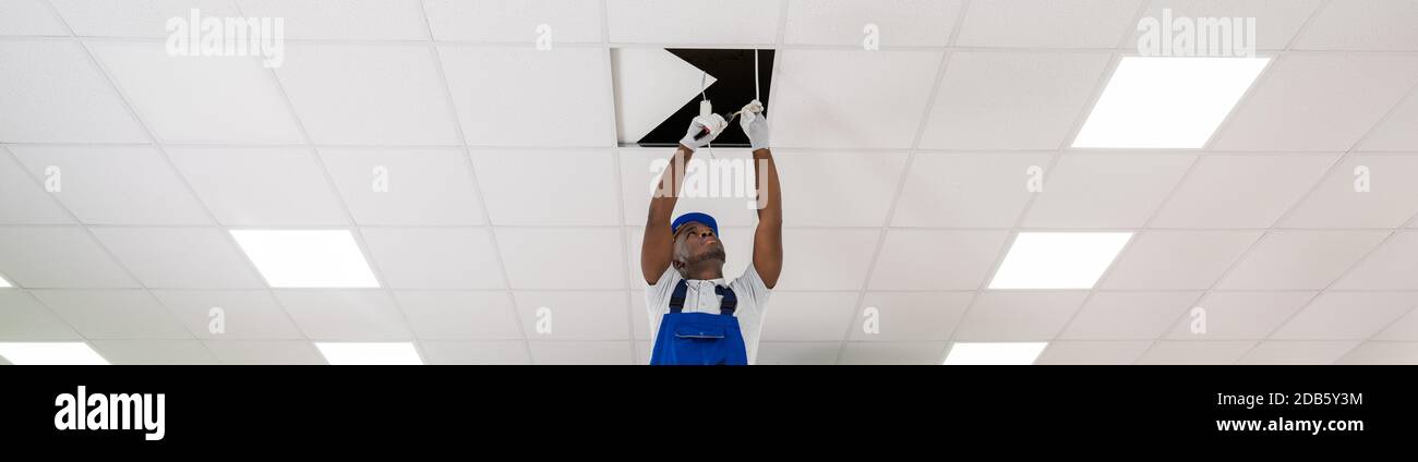 Young Male Electrician On Stepladder Installing Light On Ceiling Stock Photo