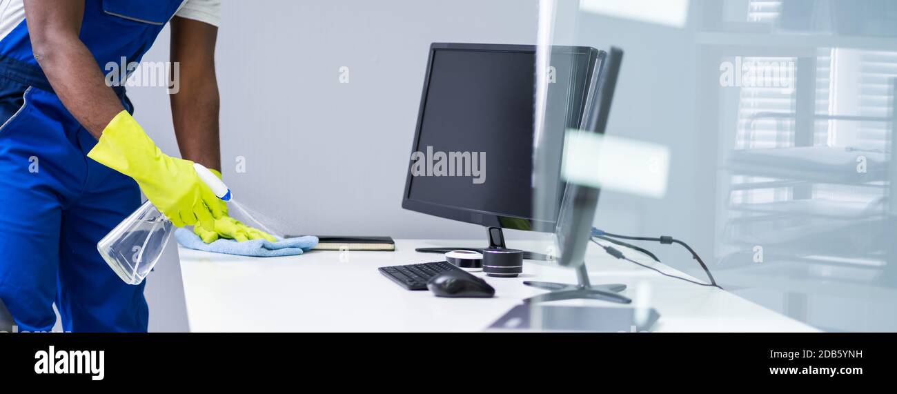 Young Male Maid Cleaning Glass Desk With Feather Duster In Office Stock