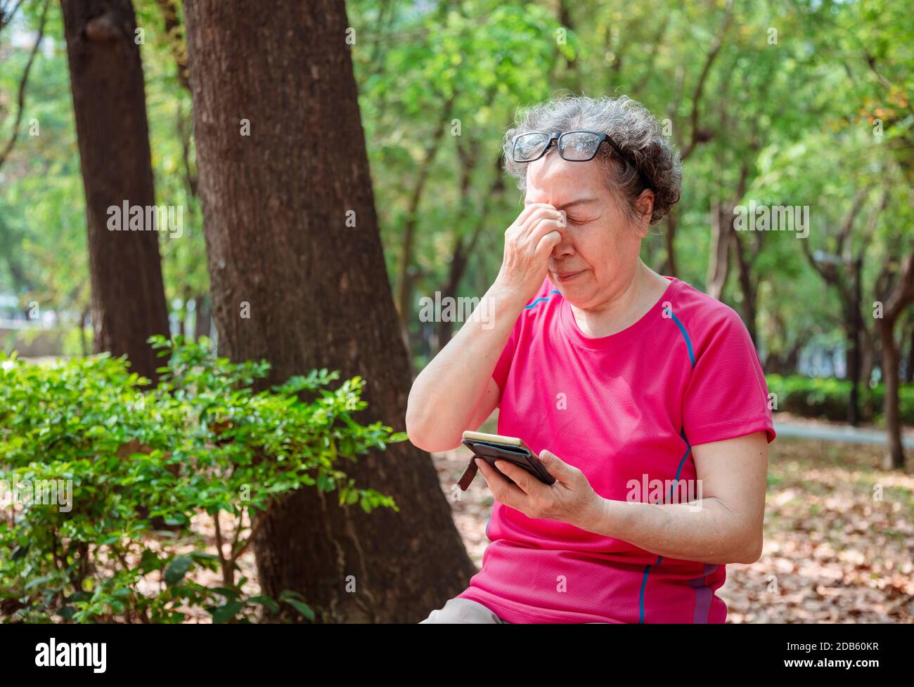 senior women have eye pain due to the use of mobile phones Stock Photo