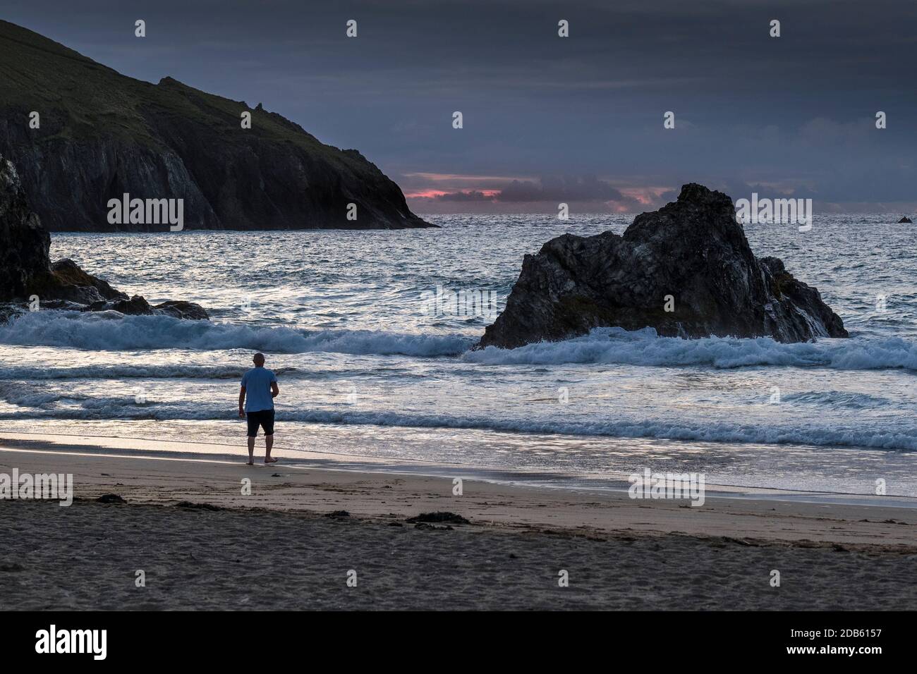 A holidaymaker standing on the shore as the sun goes down on Holywell Beach in Cornwall. Stock Photo