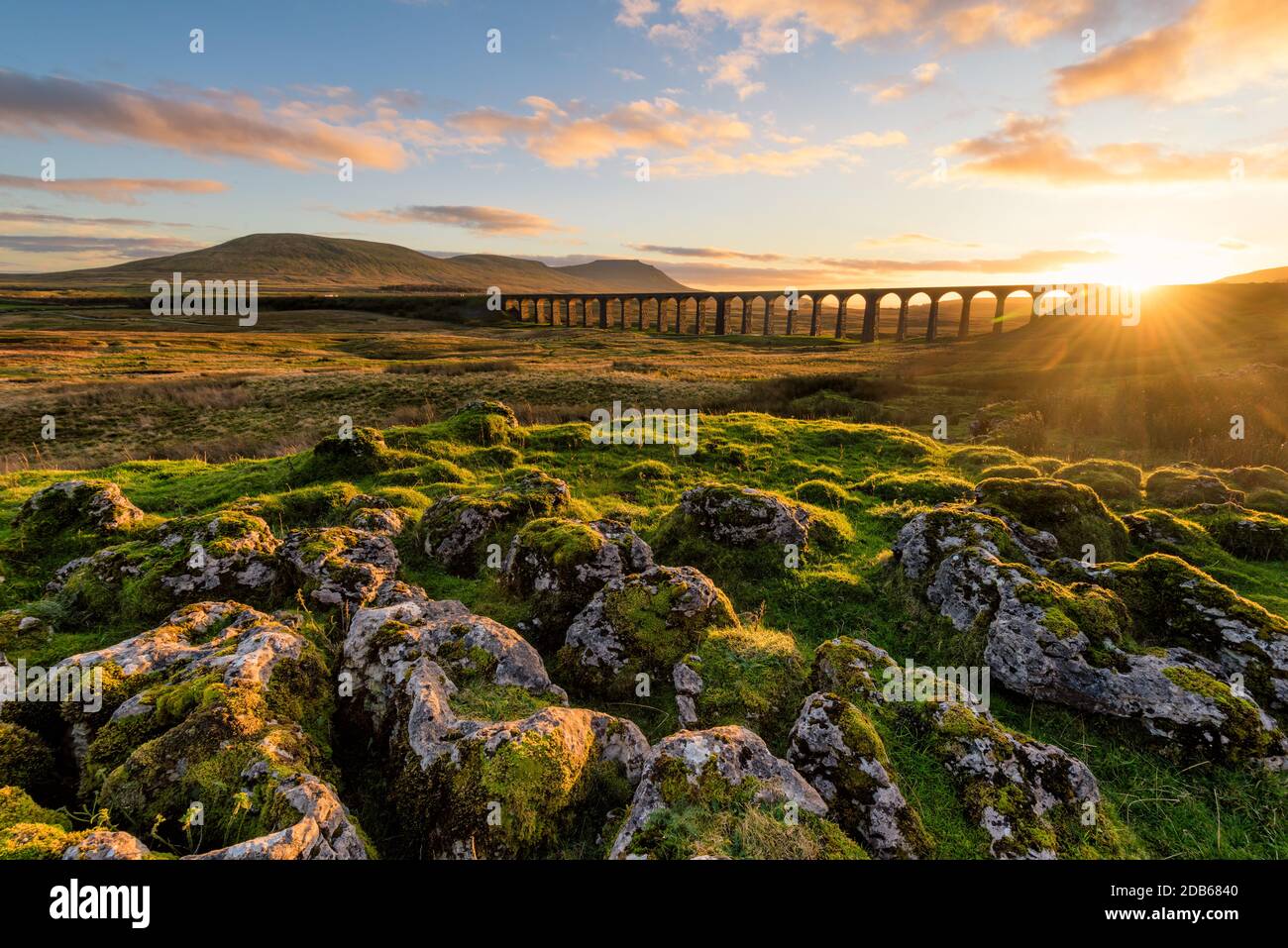 Gorgeous golden light as the sun sets behind the Ribblehead Viaduct with rocks in foreground. Stock Photo