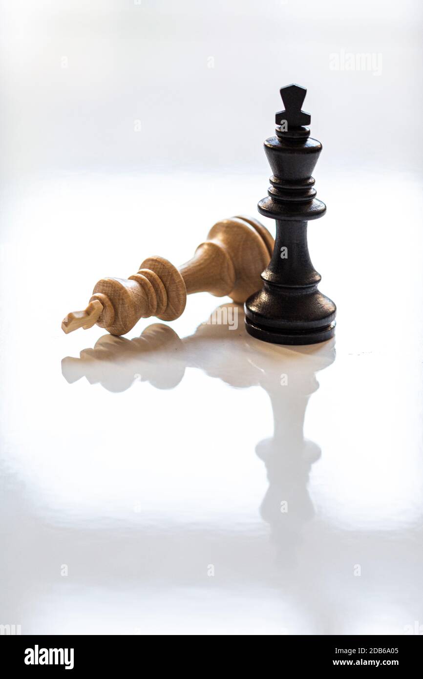 Downed white king chess piece with black king standing. Reflective surface. Vertical. Stock Photo