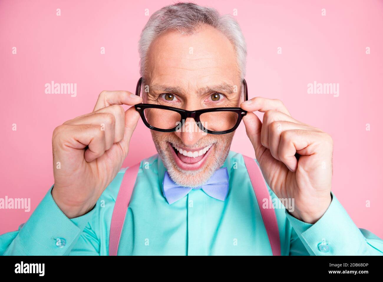 Closeup headshot photo of happy funny old man touching eyeglasses smiling laughing isolated on pink color background Stock Photo