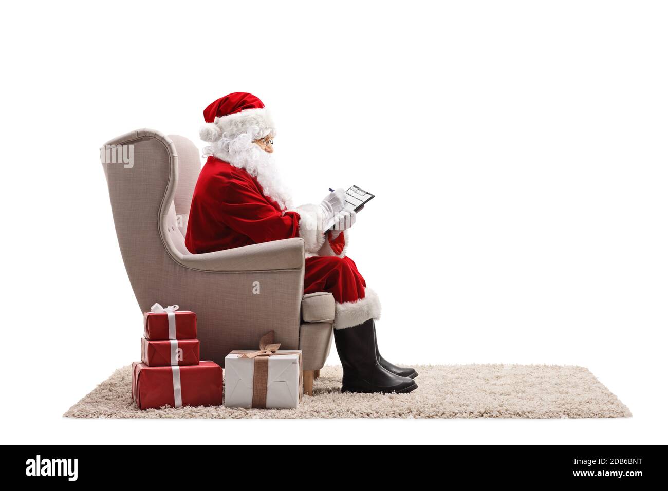 Profile shot of santa claus sitting in an armchair and writing a document isolated on white background Stock Photo
