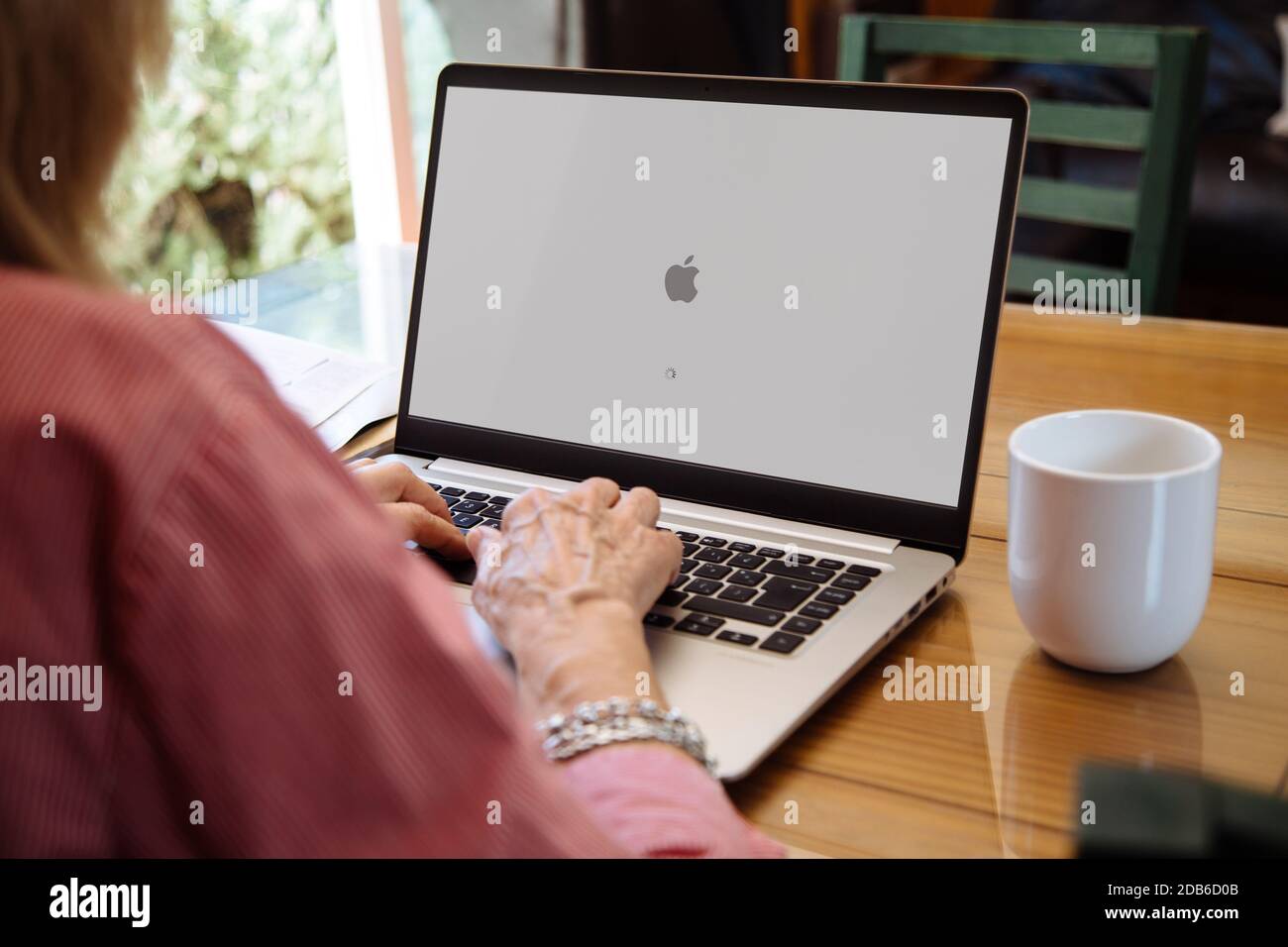 ROSARIO, ARGENTINA - NOVEMBER 16, 2020: Apple logo in the screen of laptop. Mature woman sitting in front of computer with mac os x operating system Stock Photo