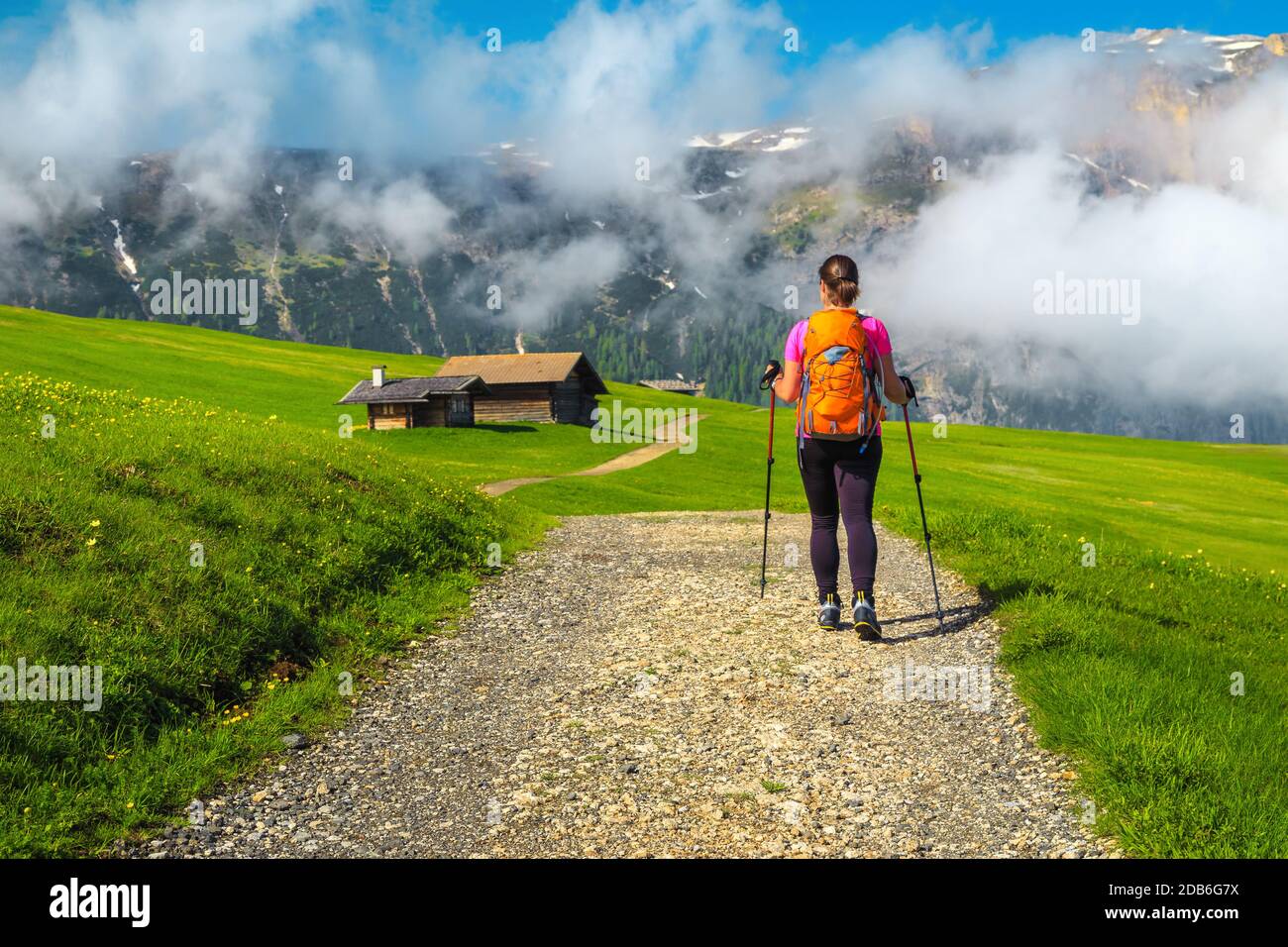 Hiking trail with wooden huts. Sporty backpacker hiker woman walking on the path in the mountains, Alpe di Siusi, Dolomites, Italy, Europe Stock Photo