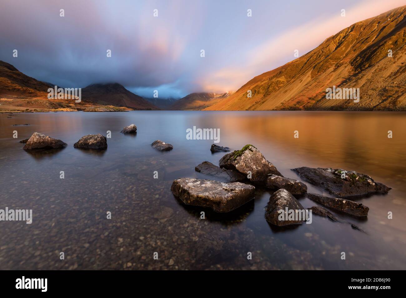 Group of rocks on the shoreline of the English Lake District's Wastwater Lake with dramatic evening winter light and moody clouds. Stock Photo