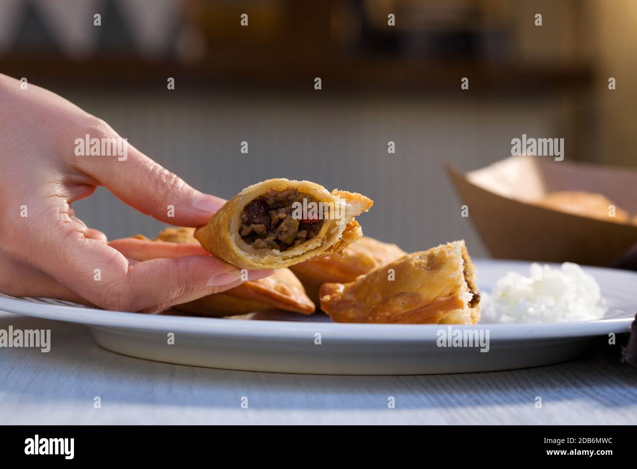 Traditional baked Argentinian empanadas savoury pastries with meat beef stuffing in woman hand on white plate. Stock Photo