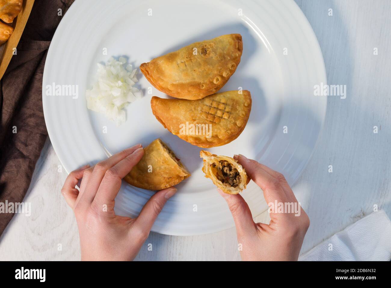Traditional baked Argentinian empanadas savoury pastries with meat beef stuffing with fresh onion on white plate from above. Stock Photo