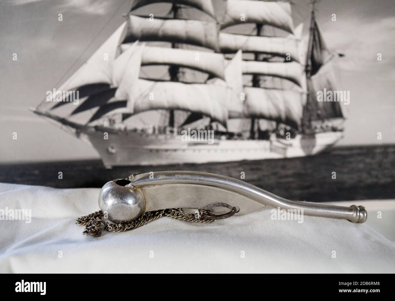 A Boatswain's whistle, or pipe, with a square-rigged sailing ship in the background. Stock Photo