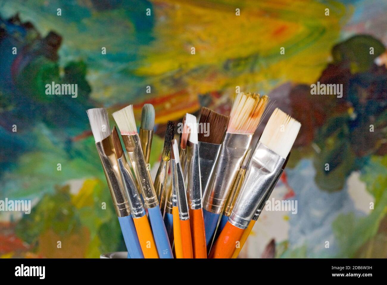 A group of different sized artist paintbrushes in a brightly colored holder in front of the painter's palette. Stock Photo