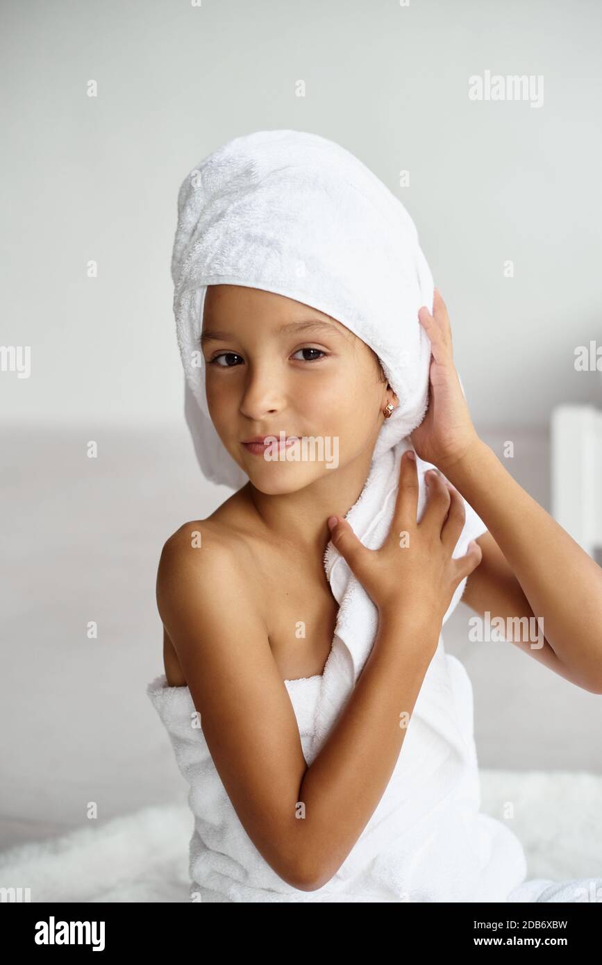 Cute girl wearing a bathrobe with wet hair after bath or shower, laughing and smiling. Little school age girl poses like a real model in a bright room Stock Photo