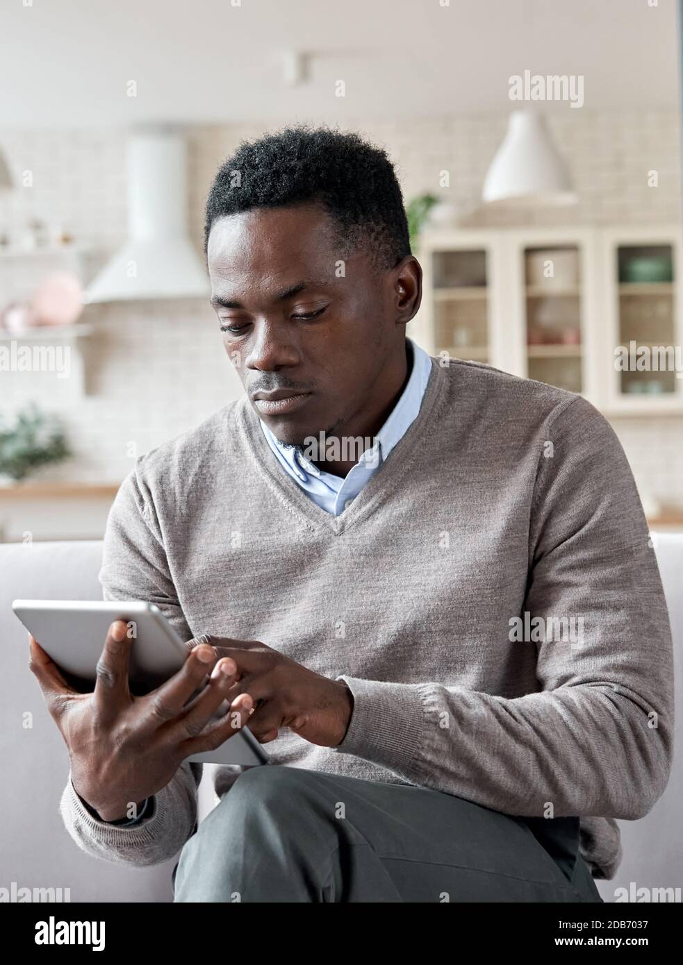 Serious african man using digital tablet apps sitting on couch at home. Stock Photo
