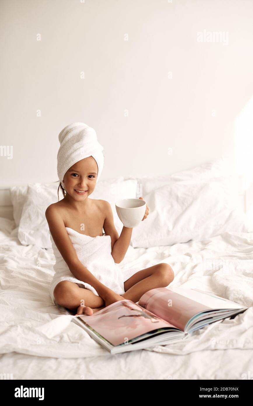 Fashion portrait of a little girl wrapped in a bath towel with a cup of