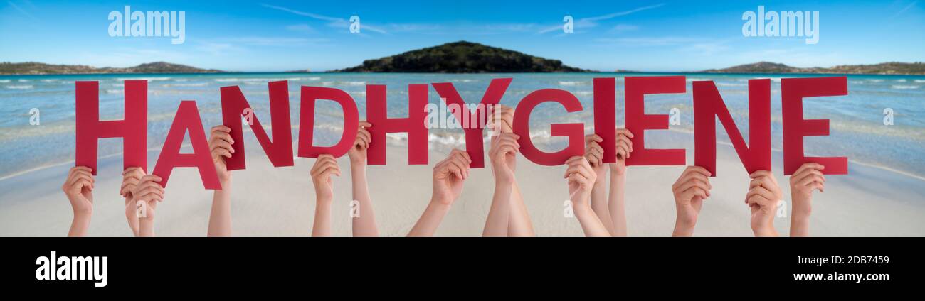 People Hands Holding Red German Word Handhygiene Means Hand Hygiene. Ocean And Beach As Background Stock Photo