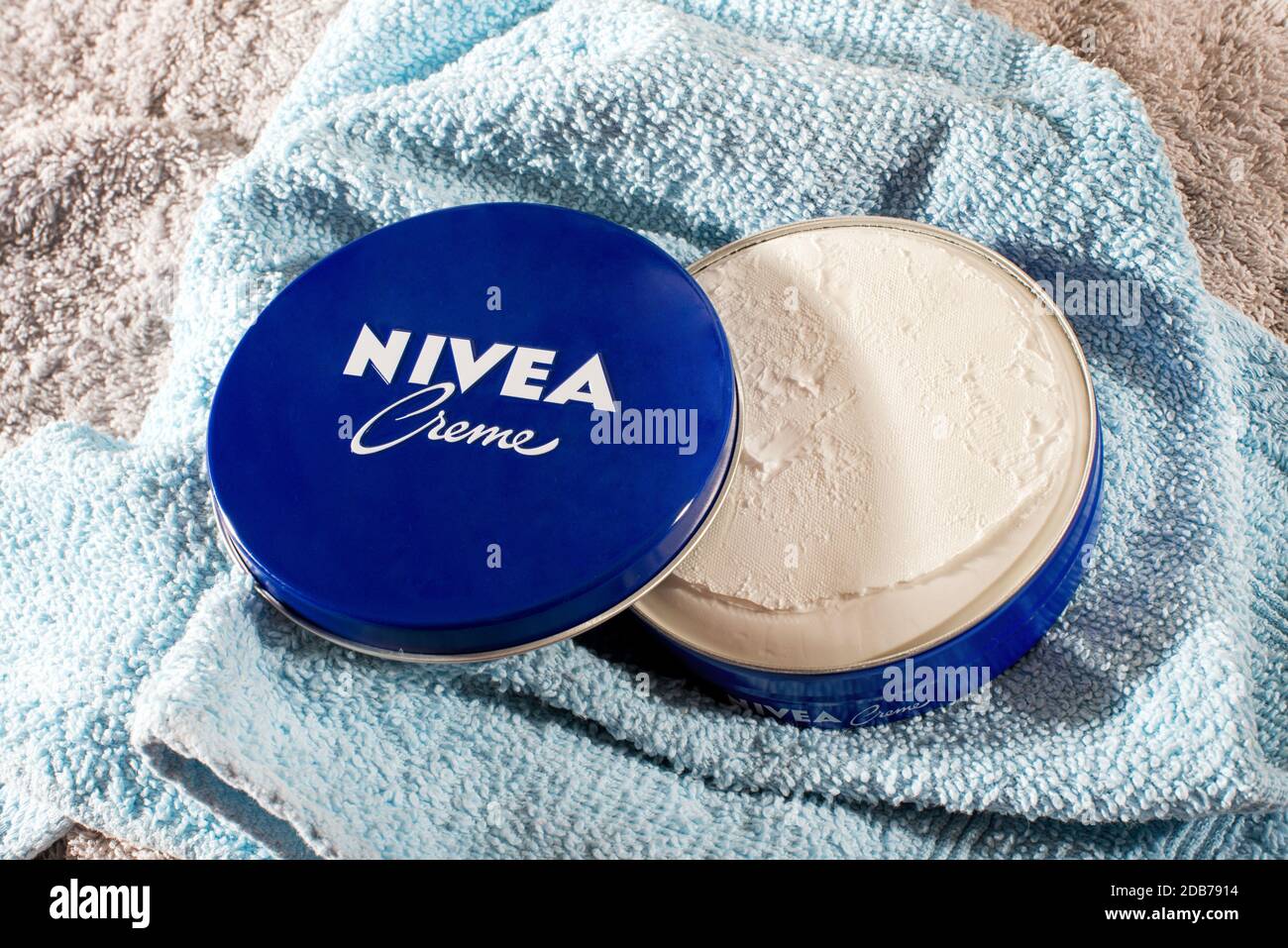 Tin of Nivea Creme showing the retail packaging opened to display the contents on a blue cotton towel Stock Photo