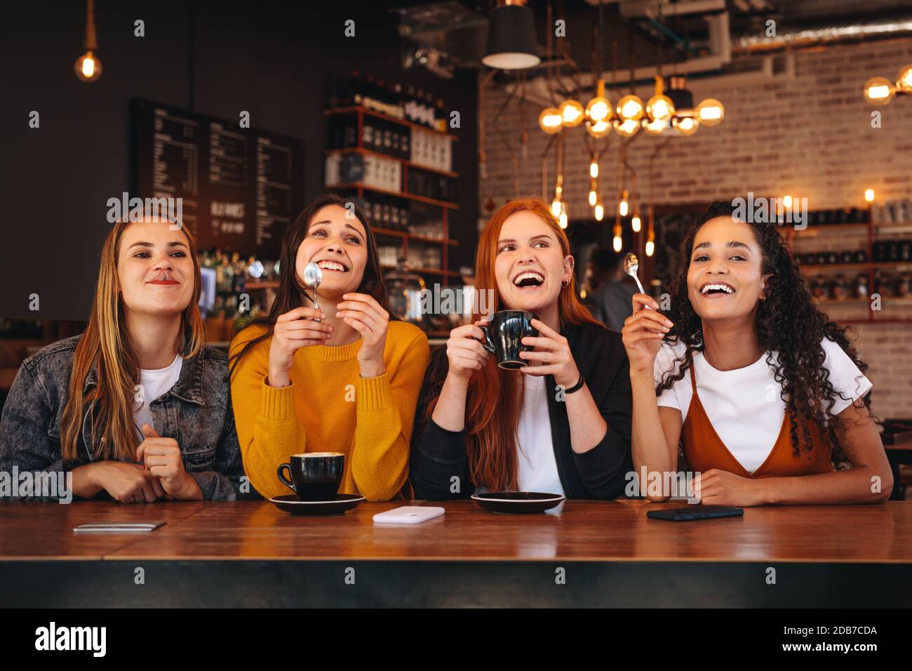Group of four women sitting at cafe looking away and laughing. Female friends having a great