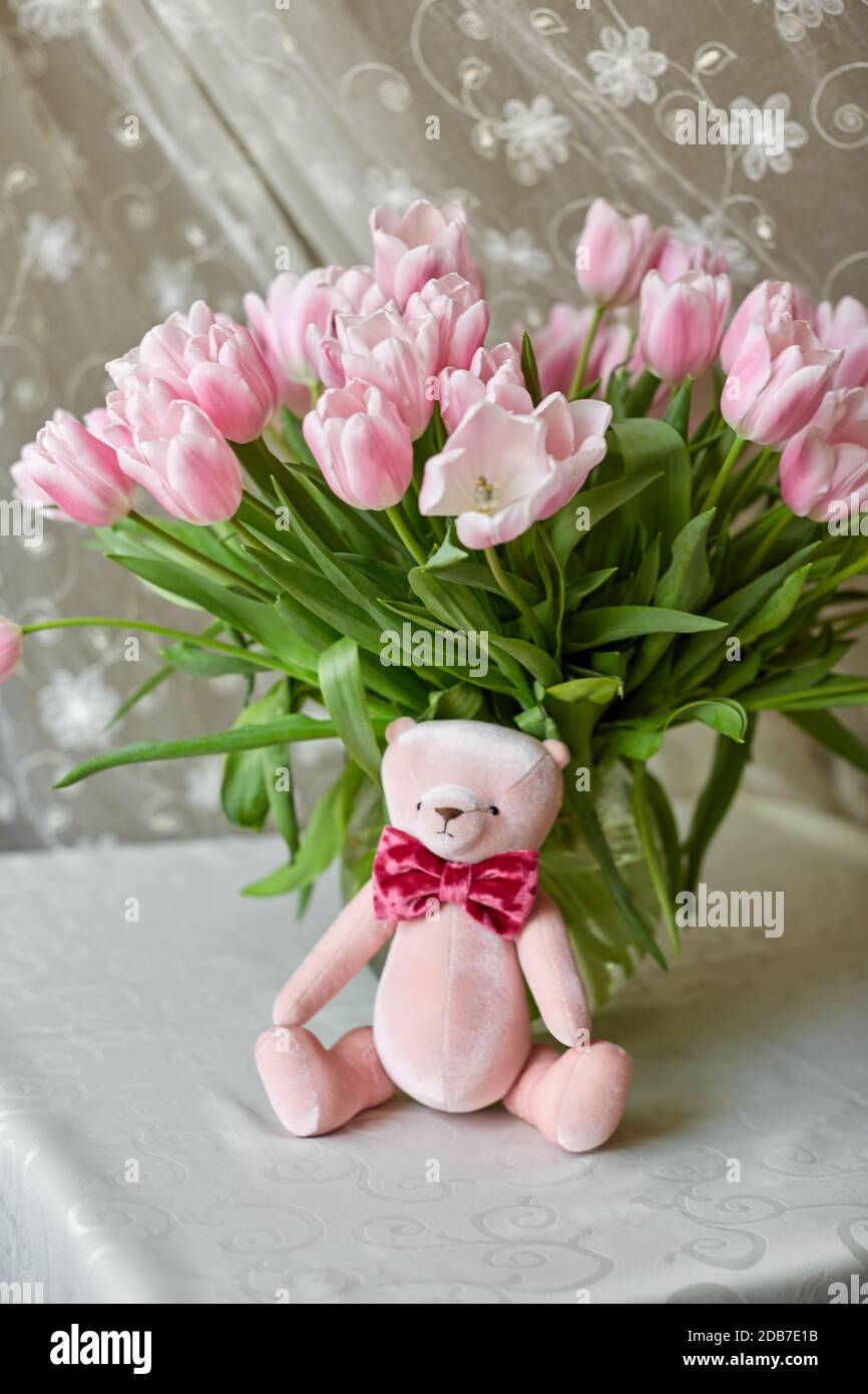 Pink bear toy and a vase with pink tulips on a table. Decor. Selective ...
